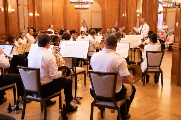 Lake Placid Sinfonietta performs under the direction of a conductor in a wood-paneled hall filled with audience members.