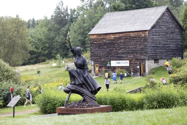 Harriet Tubman statue placed on green lawn with old barn in background and people walking on grounds