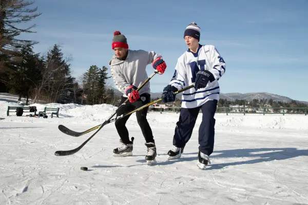 Two kids play ice hockey on a frozen lake
