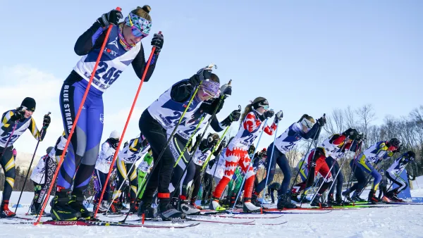 Competitors lined up for a cross-country skiing race, showcasing various athletic outfits and focused expressions on a snowy track.