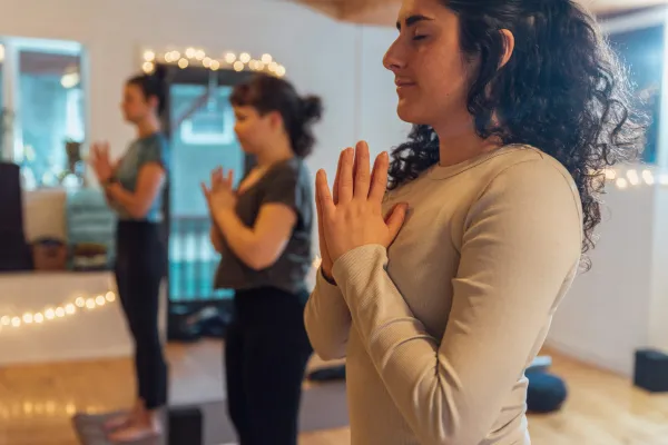 Group of people stand in yoga pose with hands pressed together at chest level in yoga studio room