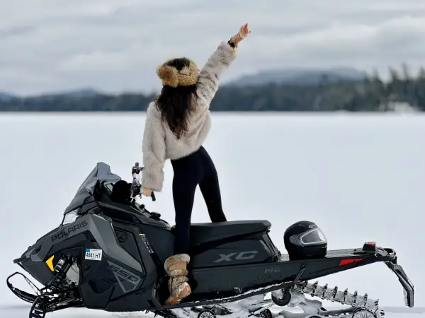 excited girl in furs looks out over the snowy landscape from atop a polaris snowmachinewith mountain backdrop