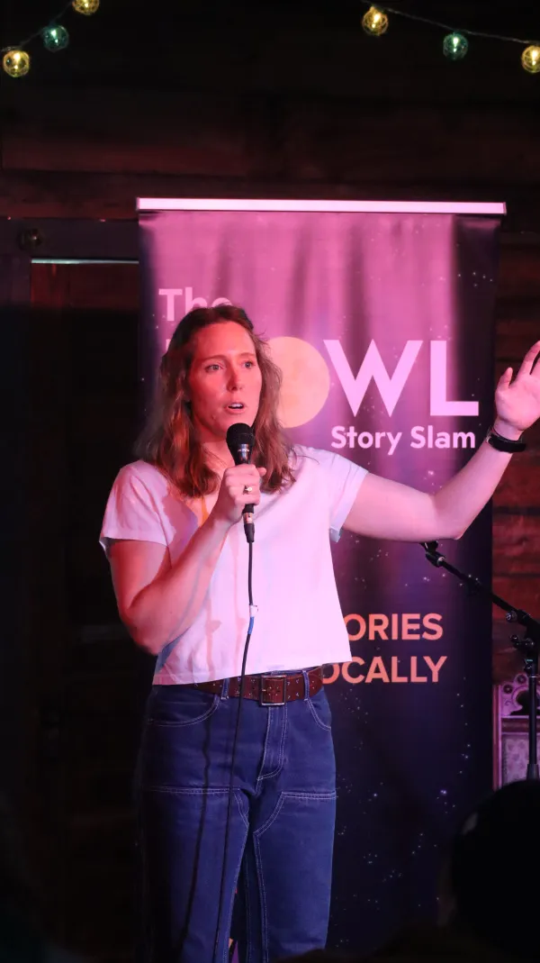 woman stands holding hand up speaking into microphone