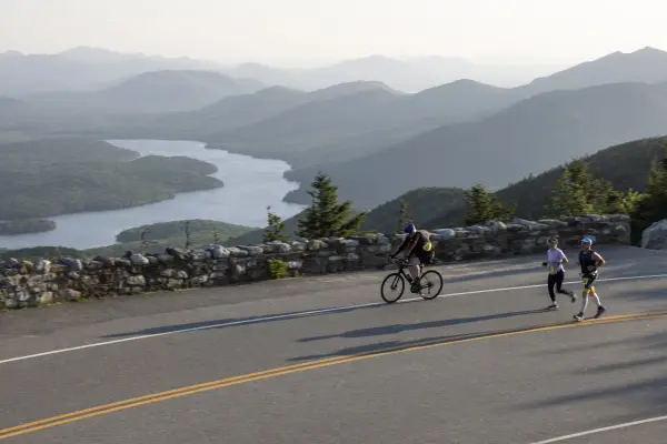 A cyclist and runners going up a road with mountain and lake views