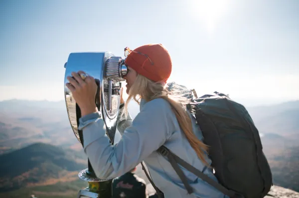 A woman looks through binoculars at a summit. 