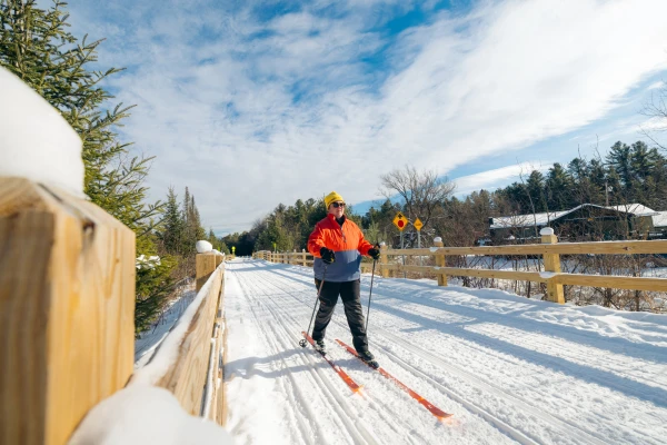 Woman cross-country skiing over long bridge on Adirondack Rail Trail on nice winter day