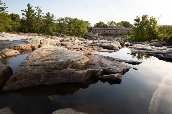 A bunch of shallow pools of water by a covered bridge