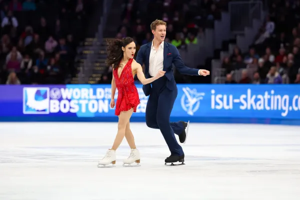 Female figure skater in a red dress and male figure skater in a blue suit perform side by side on ice