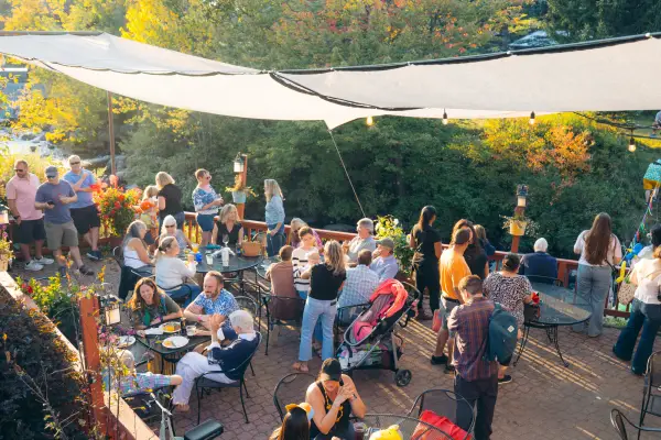 Crowd photographed from above on canopied outdoor patio sitting at tables and standing, some wearing duck accessories 