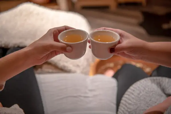 Two friends tink ceramic cups filled with nourishing herbal tea