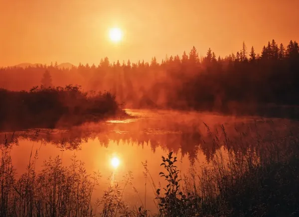 Sun low in sky over river with heavy orange haze