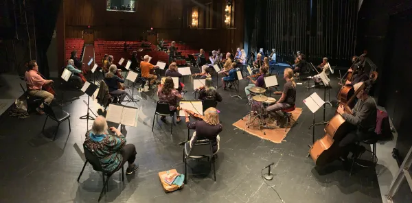 An orchestra on a stage practicing with their instruments.