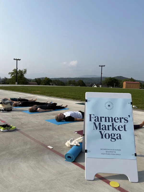 People lay on yoga mats on Olympic Oval track with mountains in distance and banner sign that says Farmers' Market Yoga