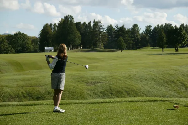 Woman in golf attire stands in backswing with golf club on green of Whiteface Club & Resort golf course