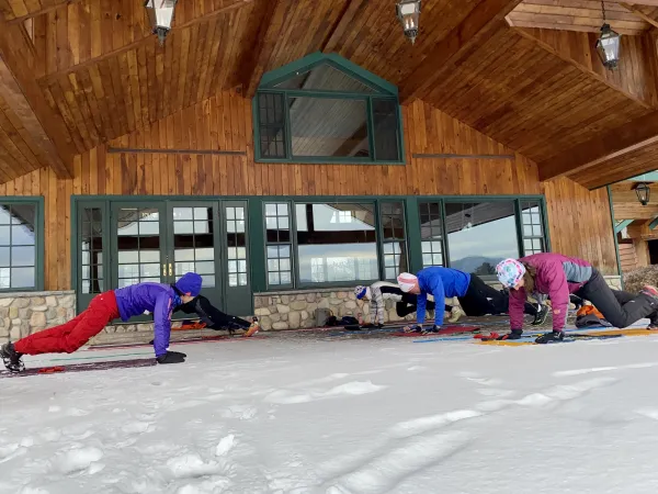 Four people doing planks outside on snow in front of a lodge.