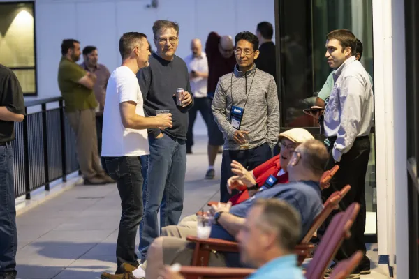 Group of peole stand talking while others sit in Adirondack chairs on deck at night