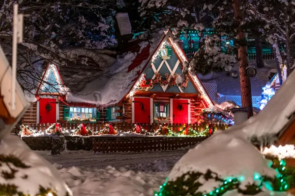 Snowy Christmas scene with a cozy, decorated log cabin glowing with festive lights. The atmosphere is warm and enchanting, surrounded by snow-laden trees.