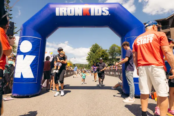 Man holding toddler crosses Ironkids finish line under blue inflatable Ironkids archway