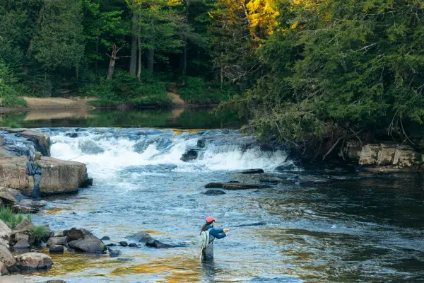 A fly fisher near a short waterfall