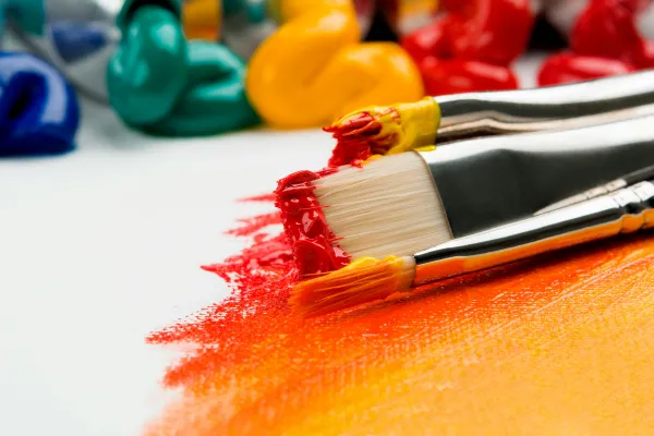Stock image of paint globs on canvas with reds and oranges painted and paint brushes covered in paint.