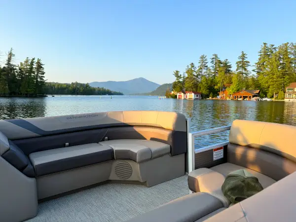 The seats of the back of a pontoon boat with glassy lake water and a misty mountain in the distance