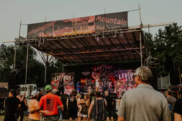Crowd of people stands looking at music festival stage outdoors in summer