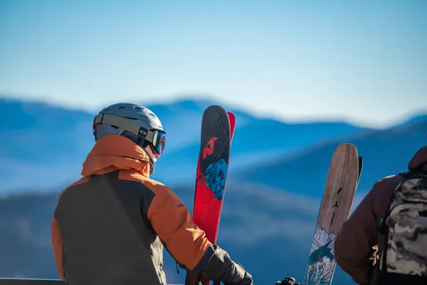 Two men in ski gear look out at a mountain range. 