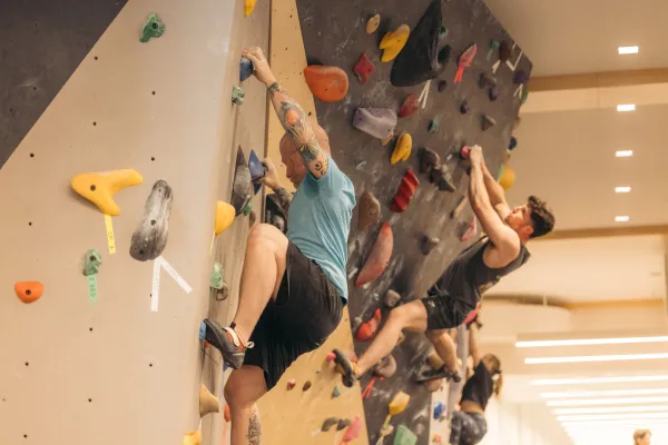 Two climbers seen side by side on indoor bouldering wall