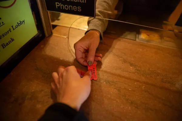 A close-up shot captures one hand passing a small "ADMIT ONE" ticket to another person across a counter at a box office.