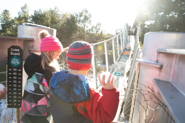 Two children play a game throwing snowballs into buckets set up on a suspended walkway on the Wild Center's Wild Walk