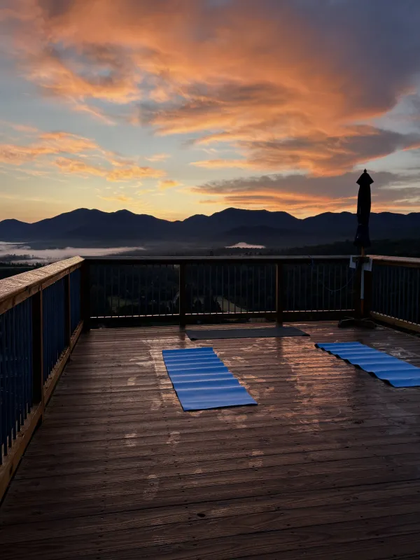 Two blue yoga mats on wooden deck with sunrise view on cloudy morning