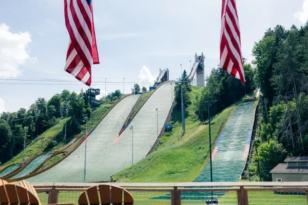 Looking up at the landing hills of the Lake Placid Ski Jumping Complex, framed by two American flags in the foreground.
