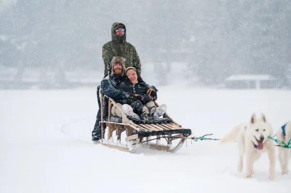 A man and woman ride a dog sled across a lake. 