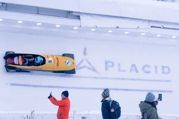 Spectators watching and taking photos of a Lake Placid bobsledding event.