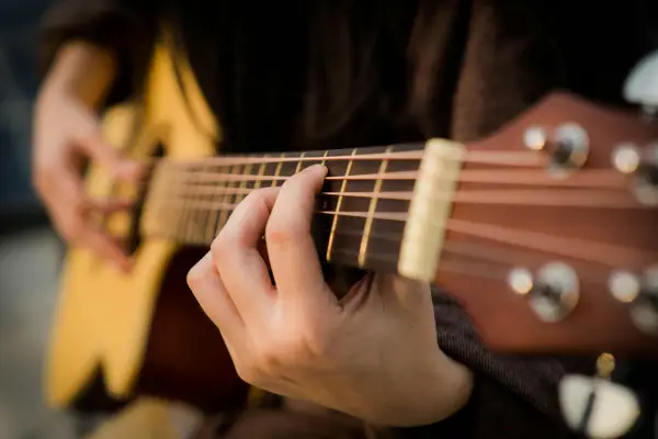 Stock image of guitar being played by person wearing black long sleeve shirt, holding chord on neck of guitar