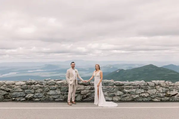 Bride and groom hold hands on Whiteface Memorial Road with mountain views behind