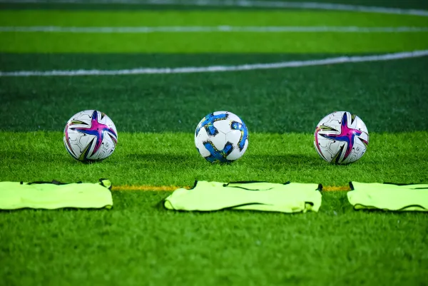 Three soccer balls on green soccer field with green pinnies laying on the ground in front of them