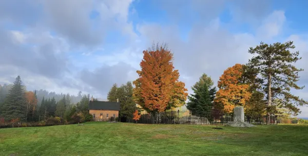 Abolitionist, John Brown's house sits on a grassy lawn, surrounded by fall foliage and a stone monument.