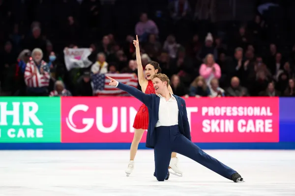 Male and female figure skating pair perform in blue suit and red dress respectively