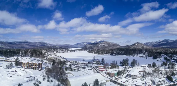 Aerial photo of the Village of Lake Placid in winter. Mirror Lake is covered in snow, as are all the buildings of downtown and the mountains in the distant background. 
