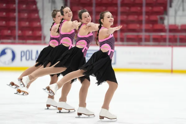 A synchronized ice skating team performs a routine in matching pink and black outfits, showcasing graceful movements on the rink.