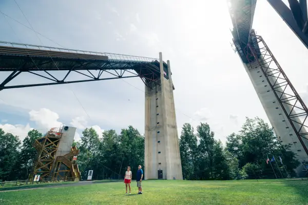 Senior couple stands on grass at the base between two towering ski jumps