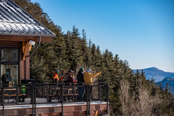 A group of skiers stand on the deck of a mountain lodge. 