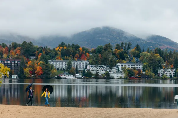 A man and woman walk on a beach on a foggy day in a small mountain town.