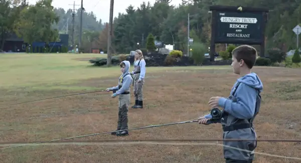 Three kids practice casting fishing rods on lawn