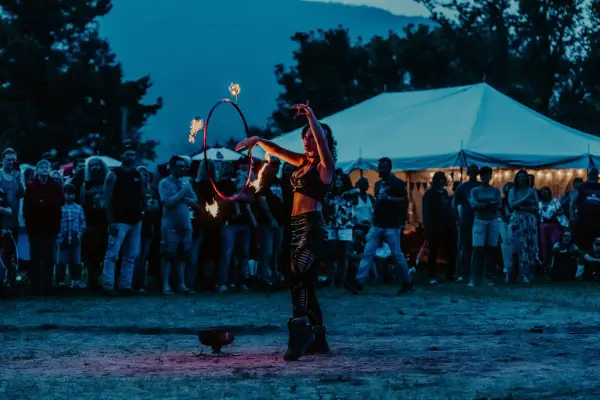 Fire dancer seen twirling flaming batons at music festival at dusk