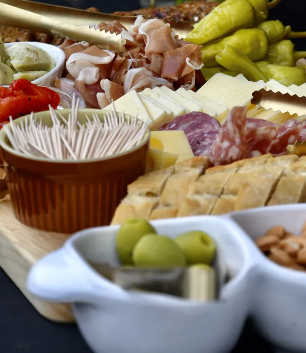 Meat and cheese charcuterie board with bread, peppers, toothpicks, and other accoutrement 