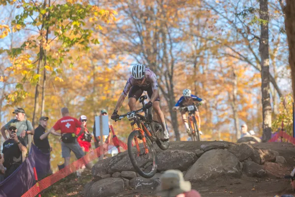 Cross-country mountain bike races rides over large rock while people look on during UCI MTB World Cup race in October