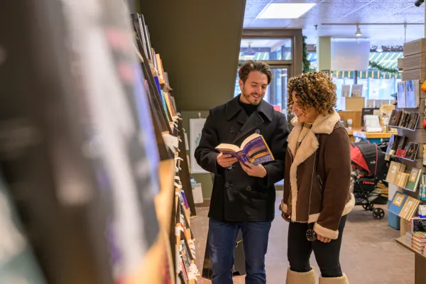 Man and woman look at open book together in aisle of bookstore