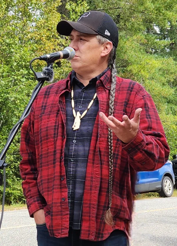 David Kanietakeron Fadden speaks into a microphone wearing a red plaid flannel